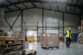 Warehouse worker maneuvering pallet jack loaded with goods through warehouse.