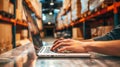 A warehouse worker types on a laptop computer in a brightly lit warehouse setting Royalty Free Stock Photo
