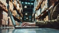 A warehouse worker types on a laptop computer in the midst of a bustling warehouse filled with stacked shelves Royalty Free Stock Photo