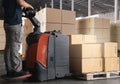 Warehouse worker working with electric forklift pallet jack unloading cardboard boxes on pallet at storage warehouse. Royalty Free Stock Photo