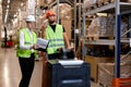 warehouse workers men in reflective jackets pulling a pallet truck and talking Royalty Free Stock Photo