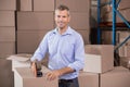 Man wearing blue shirt sealing box with tape dispenser in warehouse by metal shelving unit Royalty Free Stock Photo