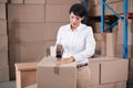 Woman working in warehouse wearing white shirt sealing boxes using tape dispenser at packing table Royalty Free Stock Photo