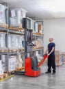 Warehouseman in storehouse moving pallet with electric stacker. Worker in warehouse stacks pallet in rack system.