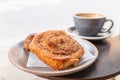 Warm cinnamon bun with icing sugar with a cup of coffee lying on the table in a street cafe