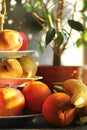 Warm color sunlit pears apples oranges and bananas fruits on three tier porcelain stand server next to a ficus pot plant Royalty Free Stock Photo