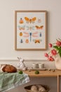 Warm composition of easter living room interior with mock up poster frame, wooden sideboard, vase with tulips, easter bunny, bread