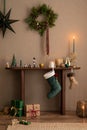 Warm and cozy composition of christmas living room interior with christmas wearth, wooden console, candle, brown wall, christmas