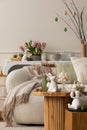 Warm and cozy composition of easter living room interior with coffee table, white sofa, colorful easter eggs, easter bunny, Royalty Free Stock Photo