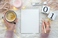 Warm cozy home start new year 1 january on perpetual calendar. Notebook mockup and woman hands holds gold penand cup of