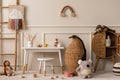 Warm and cozy kids room interior with white desk, stool, animal wicker basket, rattan sideboard, stylish toys, plush monkey, koala