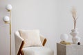 Warm and cozy living room with white armchair, lamp, consola and personal accessories. Beige wall. Home decor. Template