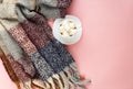 Warm, cozy winter scarf and white cup of coffee with white marshmallow as frame on pastel pink background.