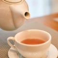Warm cup of tea being poured from white teapot into a cup on a saucer in a cozy Royalty Free Stock Photo