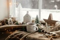 Warm cup of tea, christmas decor and lights on cozy blanket at window. Christmas Winter hygge