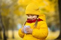 Warm fall photo. Close-up shot of a pretty cute little child girl wearing bright yellow coat and cap, holding a cup of Royalty Free Stock Photo