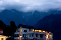 The warm lights from a building against the cool backdrop of fog covered mountains in the hill station of McLeodganj