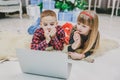 Warm photo of pretty siblings watching new year movie while laying on the carpet under Christmas fir. Royalty Free Stock Photo