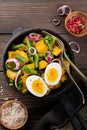 Warm potato salad with green beans, pepper, parsley, eggs and red onion in frying pan on old wooden background. Selective focus. Royalty Free Stock Photo