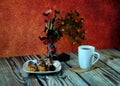 Warm still life, a plate with fresh eclairs, a white ceramic mug with tea on a napkin and a glass vase with an autumn herbarium