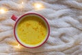 Warm winter drink spiced golden turmeric milk on beige woolen knitted background with fairy lights