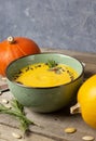 Warming autumn cream pumpkin soup in a green bowl. Pumpkins, rosemary twigs, pumpkin seeds on a wooden table