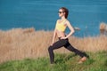 Warming up before jogging. Attractive young woman in sports clothing and sunglasses doing stretching exercises and looking concent Royalty Free Stock Photo