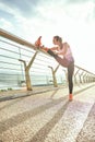 Warming up before run. Side view of disabled positive woman in sportswear and headphones stretching prosthetic leg while Royalty Free Stock Photo