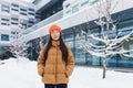 Warmly dressed asian girl walking down the street on a winter snowy day, portrait of a woman in a jacket and orange warm hat Royalty Free Stock Photo