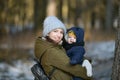 Warmly dressed mom and baby are walking along the street. Mom holds a baby in her arms in winter. Mom and son outdoors in winter. Royalty Free Stock Photo