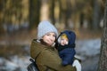 Warmly dressed mom and baby are walking along the street. Mom holds a baby in her arms in winter. Mom and son outdoors in winter. Royalty Free Stock Photo