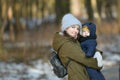 Warmly dressed mom and baby are walking along the street. Mom holds a baby in her arms in winter. Mom and son outdoors in winter. Royalty Free Stock Photo