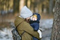 Warmly dressed mom and baby are walking along the street. Mom holds a baby in her arms in winter. Mom and son outdoors in winter. Royalty Free Stock Photo