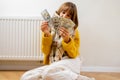 Warmly dressed woman counting money near radiator