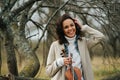 Warmly dressed woman with violin over leafless autumn lichen-covered trees