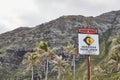 Warning Dangerous shore break sign on a beach with palm trees and mountain in the background