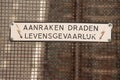 Warning on fence above electricity cables for trains that touching is life-threatening aanraken dragen levensgevaarlijk