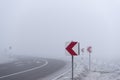 Warning road signs before dangerous curve in dense mist Royalty Free Stock Photo