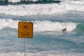 Warning sign of closed beach with person surfing rough waves on the background