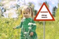 Warning sign: danger allergy season. a little girl in a blue dress walks along the field with flowers on a sunny summer day Royalty Free Stock Photo
