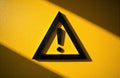 Warning sign with exclamation mark on yellow wall creating shadow effect Royalty Free Stock Photo