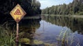 A warning sign near a polluted lake cautioning against swimming or drinking due to acid rain contamination