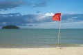 Warning sign of a red flag at a beautiful clean beach with a blue sky, cloud and the sea with small green island Royalty Free Stock Photo