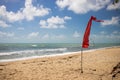 Warning sign of a red flag at a beautiful empty tropical beach with a blue sky and sea Royalty Free Stock Photo