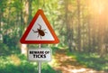 Warning sign with text BEWARE OF TICKS, against defocused forest background Royalty Free Stock Photo