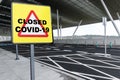 Warning sign with text CLOSED COVID-19 on a empty parking lot of an airport or train station
