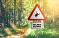 Warning sign with text ZECKEN GEFAHR, German for beware of ticks, against defocused forest background