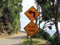 Warning Sign to Blow Horn Before Treacherous 90 Degree Turn on Narrow Road with Cliff Beside Ocean