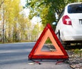 Warning stop sign on the road against the background of a white car and forest. concept of roadside assistance, travel incidents,