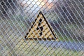 Warning triangular sign on a gray iron shallow grid of a fence